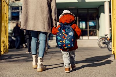 Das Bild zeigt die Rückansicht eines Kindes an der Hand eines Elternteils vor dem Eingang einer Kindertageseinrichtung.