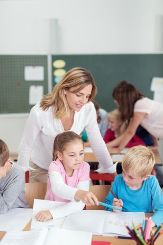 Bild zeigt eine Lehrerin die hinter zwei sitzenden Kindern über deren Köpfe schaut